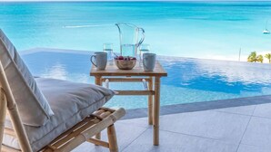 A wooden table with a bowl of fruit, two pitchers, and glasses on a balcony overlooking a clear blue sea. - Panorama Suite – Oceanview Luxury Suite at Tamarind Hills, Antigua (Unknown)