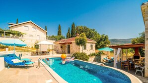 A swimming pool with lounge chairs, a sun umbrella, and a stone building in the background. - Dubrovnik Chalets (Konavle)