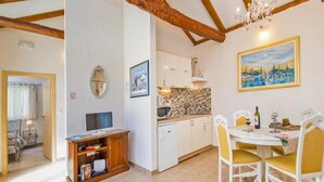 A cozy kitchen with white cabinets, a tiled backsplash, and a dining area with yellow chairs and a white table. - Dubrovnik Chalets (Konavle)