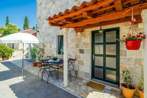 Ein Steinhaus mit einer Holzpergola, Sitzmöglichkeiten im Freien und Kübelpflanzen.
