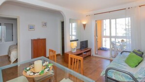 Een gezellige woonkamer met een glazen tafel, een bank, een televisie en een schuifpui naar een balkon.