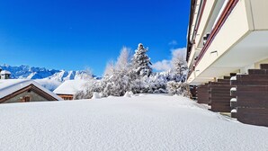 Un carrer cobert de neu amb un edifici a la dreta i muntanyes al fons.