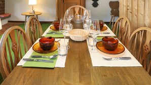 Taula de menjador preparada amb plats, gots i coberts, envoltada de cadires de fusta.
