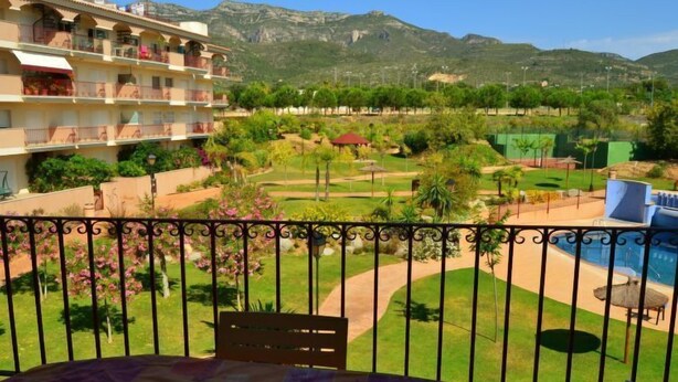 A balcony with a view of a landscaped garden, a pool, and a mountain backdrop. - Golden Beach by Interhome (St Carles de la Ràpita)