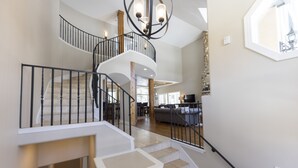 Un interior espacioso con una escalera curva, un candelabro y vistas a un salón.