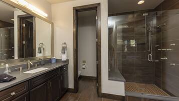 A modern bathroom with a large mirror, dual sinks, a shower enclosure, and dark wood cabinetry.
