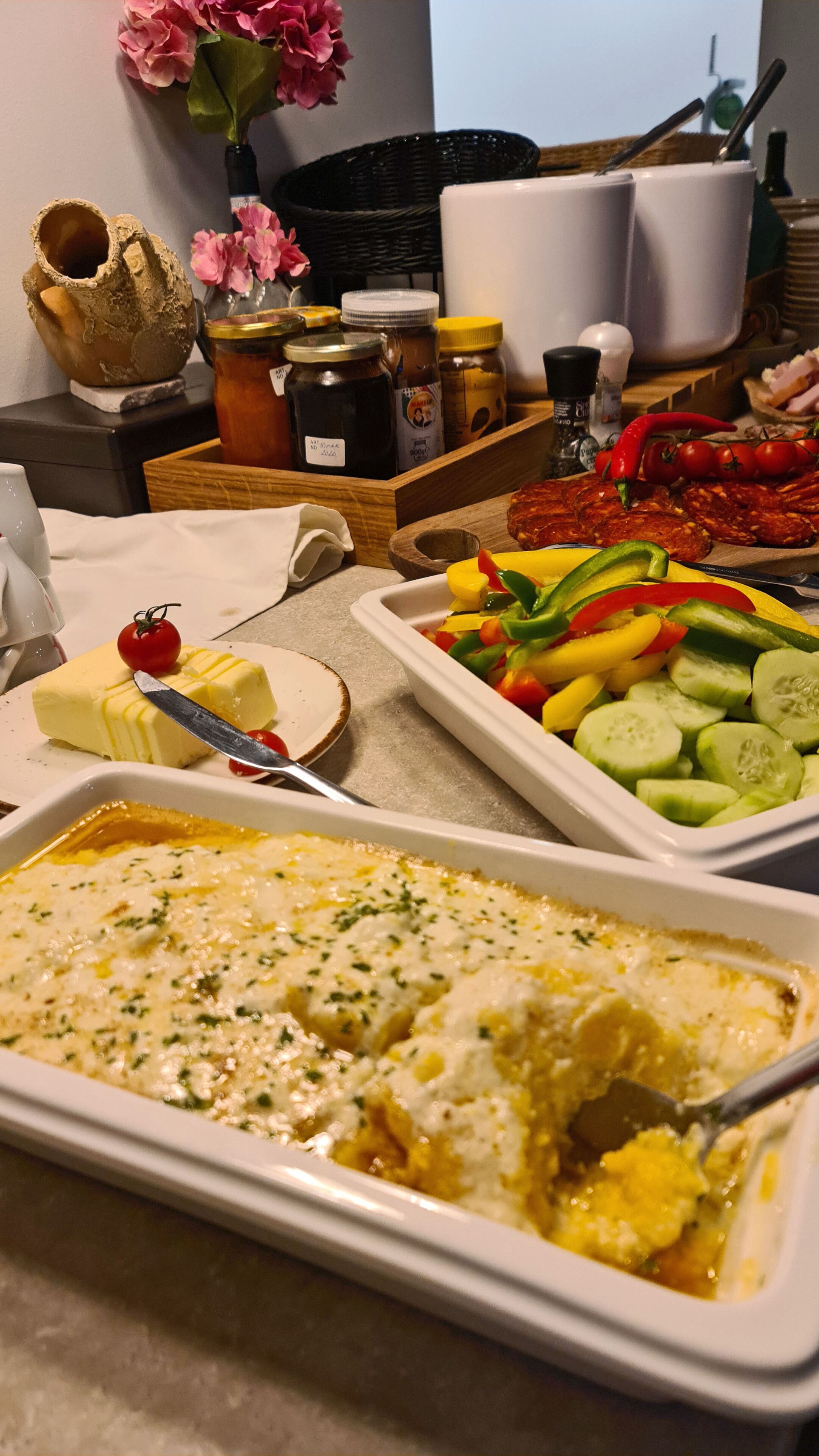 A buffet table with various dishes including a casserole, sliced vegetables, and a spread of meats.