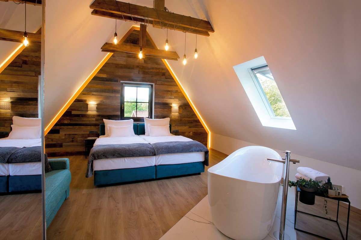 A bedroom with two beds, a skylight, a large bathtub, and wooden paneling on the walls.