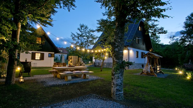 A rustic cabin with a picnic table and string lights, surrounded by trees and a well-maintained lawn. - Plitvice Holiday Lodge (Plitvicka Jezera)