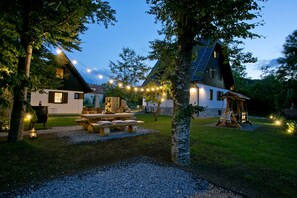 Un chalet rustique doté d’une table de pique-nique et de guirlandes lumineuses, entouré d’arbres et bordé d’une pelouse bien entretenue.