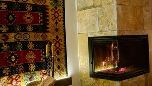 A room with a stone wall, a fireplace, a woven basket, and a colorful rug. - Plitvice Holiday Lodge (Plitvicka Jezera)