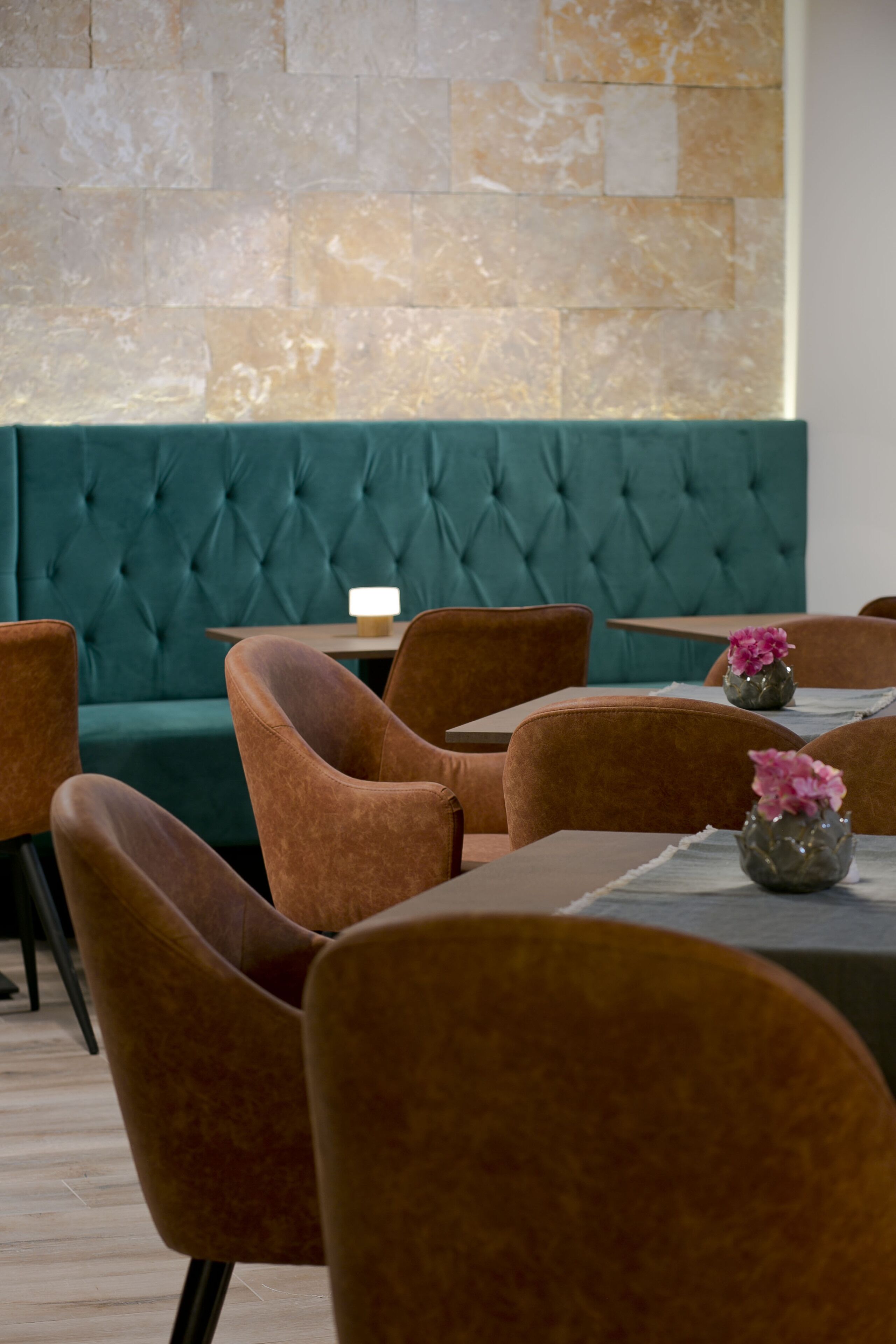 Un interior de restaurante con cabinas tapizadas en color verde azulado, sillas marrones y mesitas.