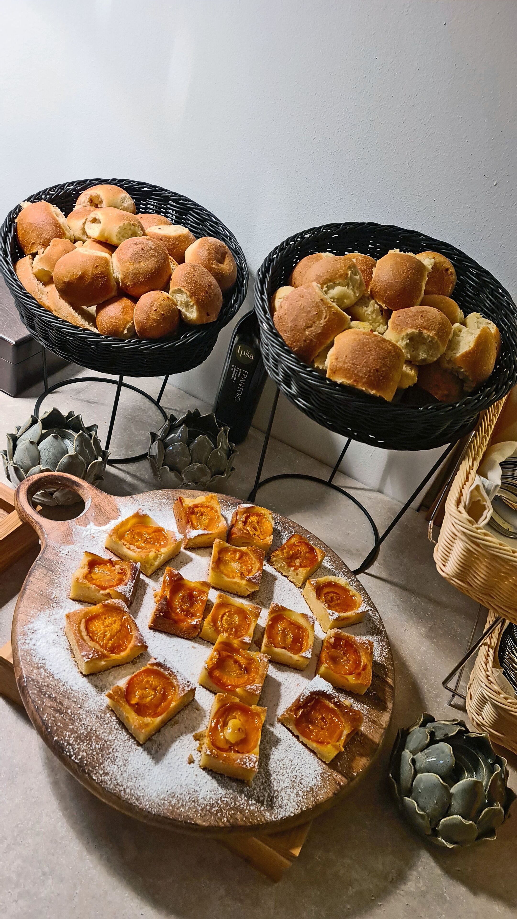 Una mesa con cestas de panecillos y un plato de pasteles cuadrados espolvoreados con azúcar glas.
