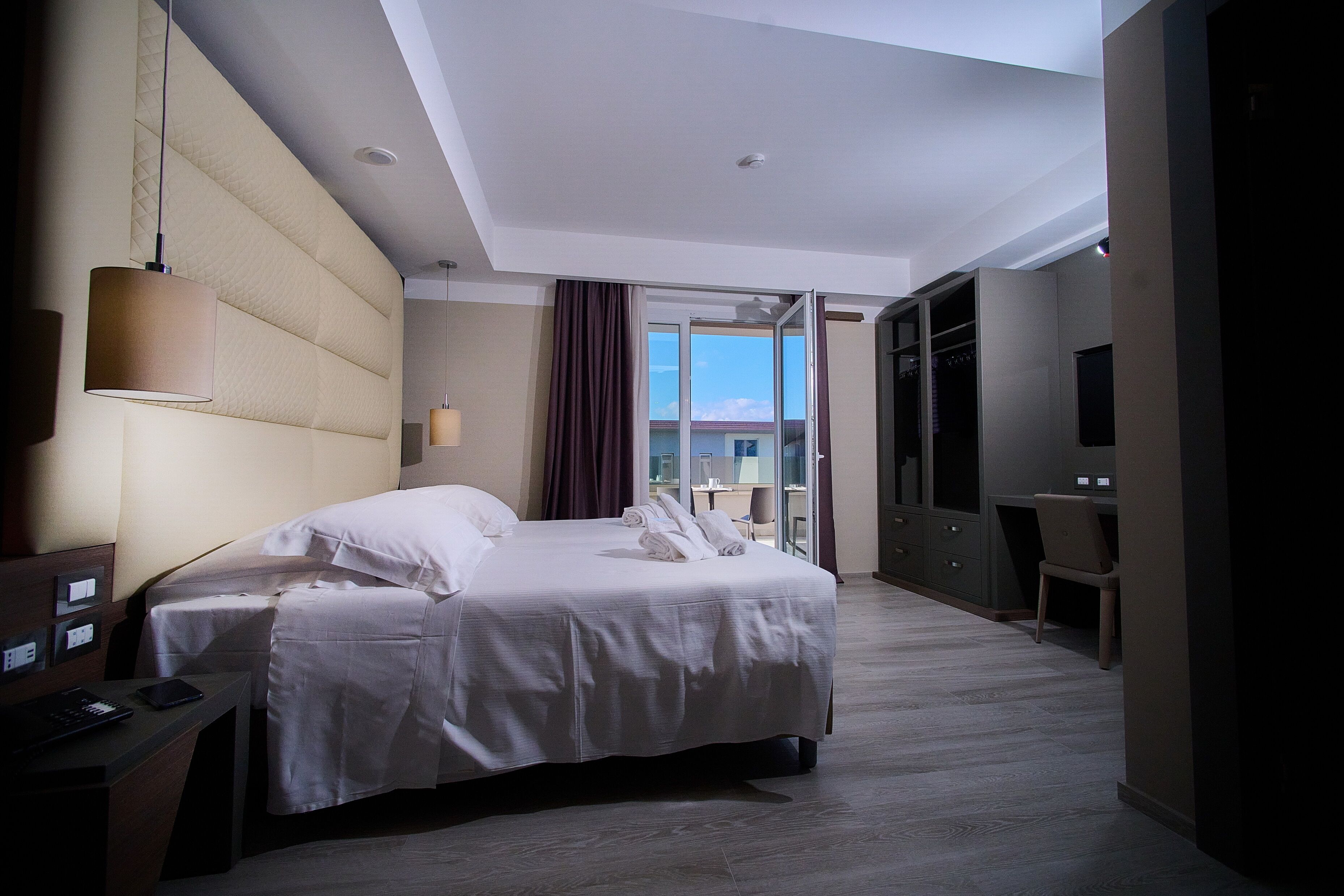 A hotel room with a bed, a desk, a chair, a TV, and a view of the outdoors.