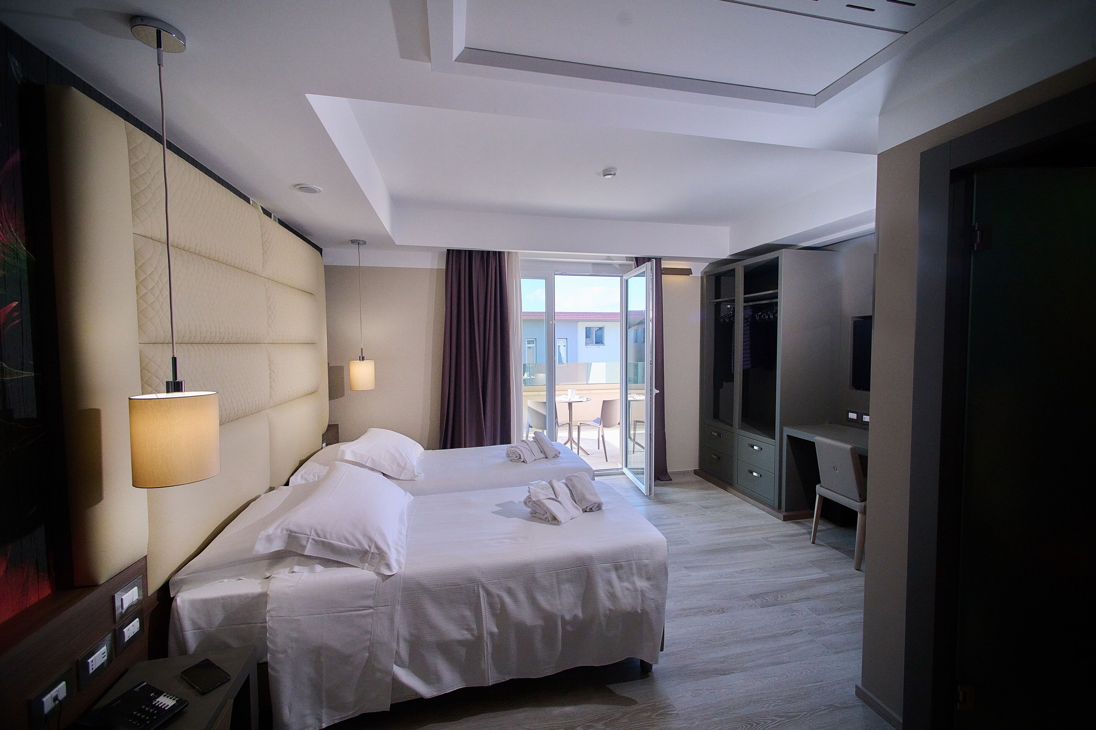 A hotel room with two beds, a desk, a TV, and a balcony with a view.