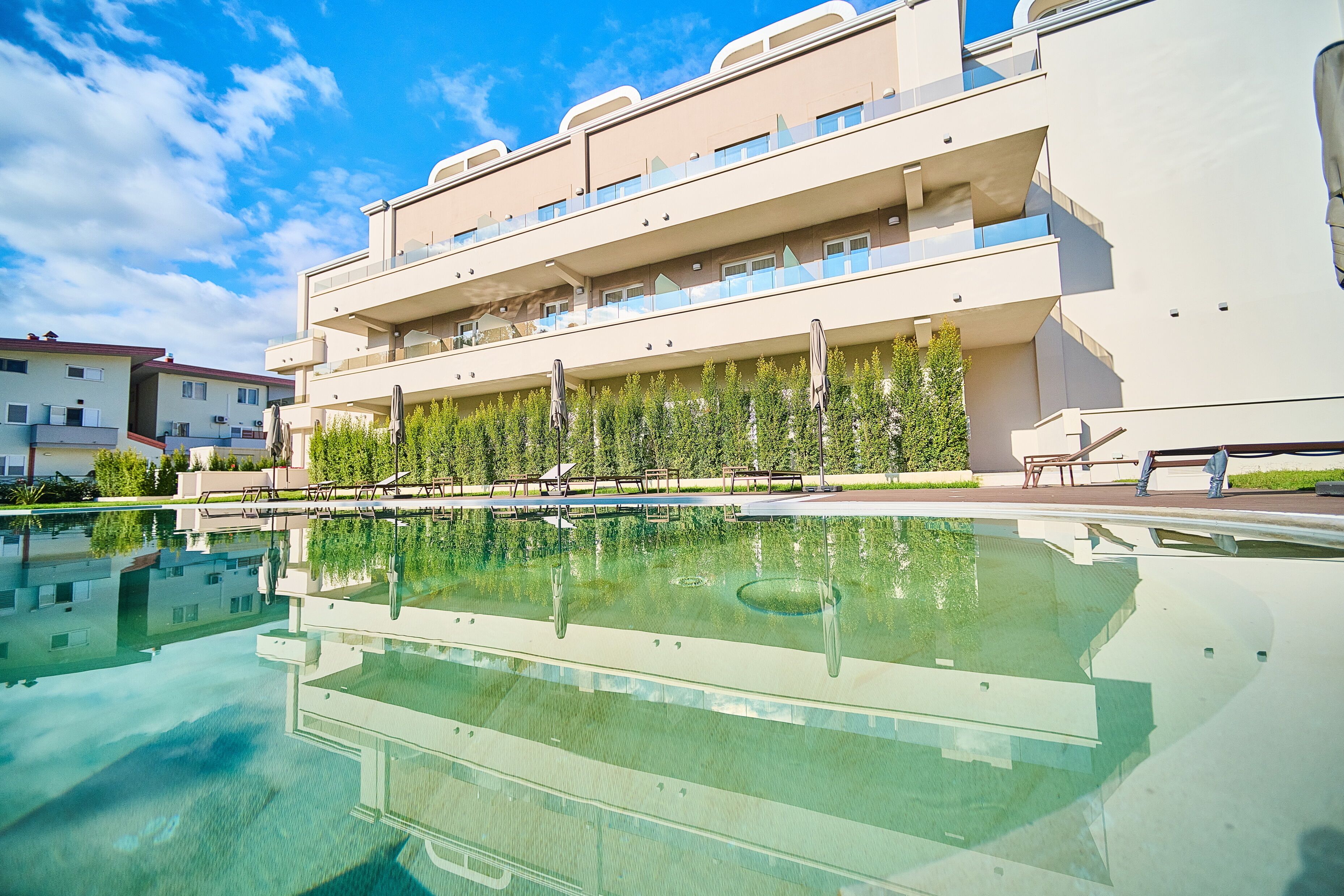 Ein modernes Hotel mit Pool, mehreren Balkonen und blauem Himmel.