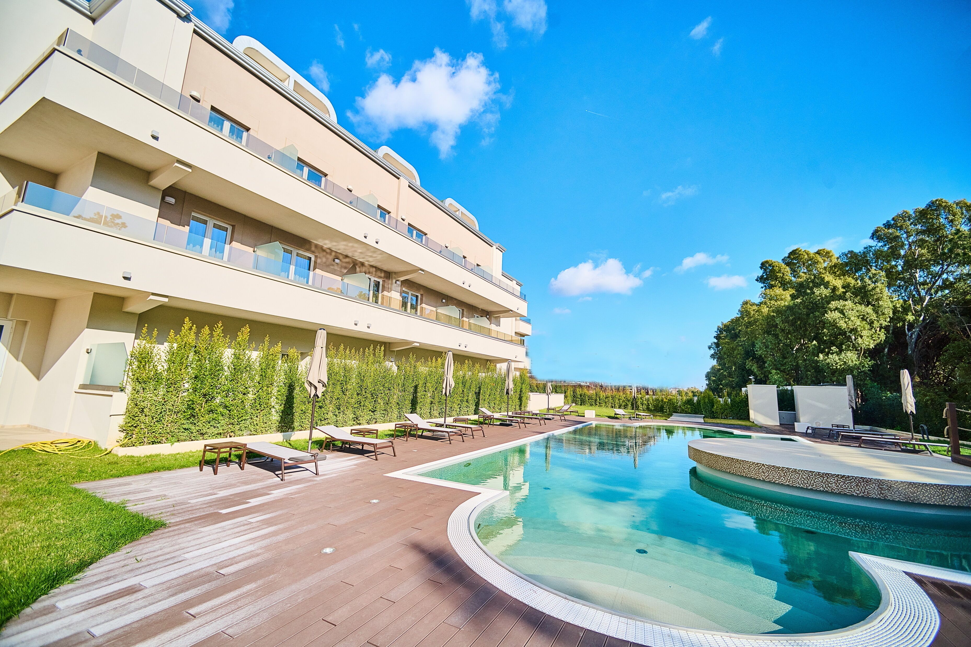 Ein modernes Hotel mit Poolbereich, Sitzgelegenheiten im Freien und einem gepflegten Garten.
