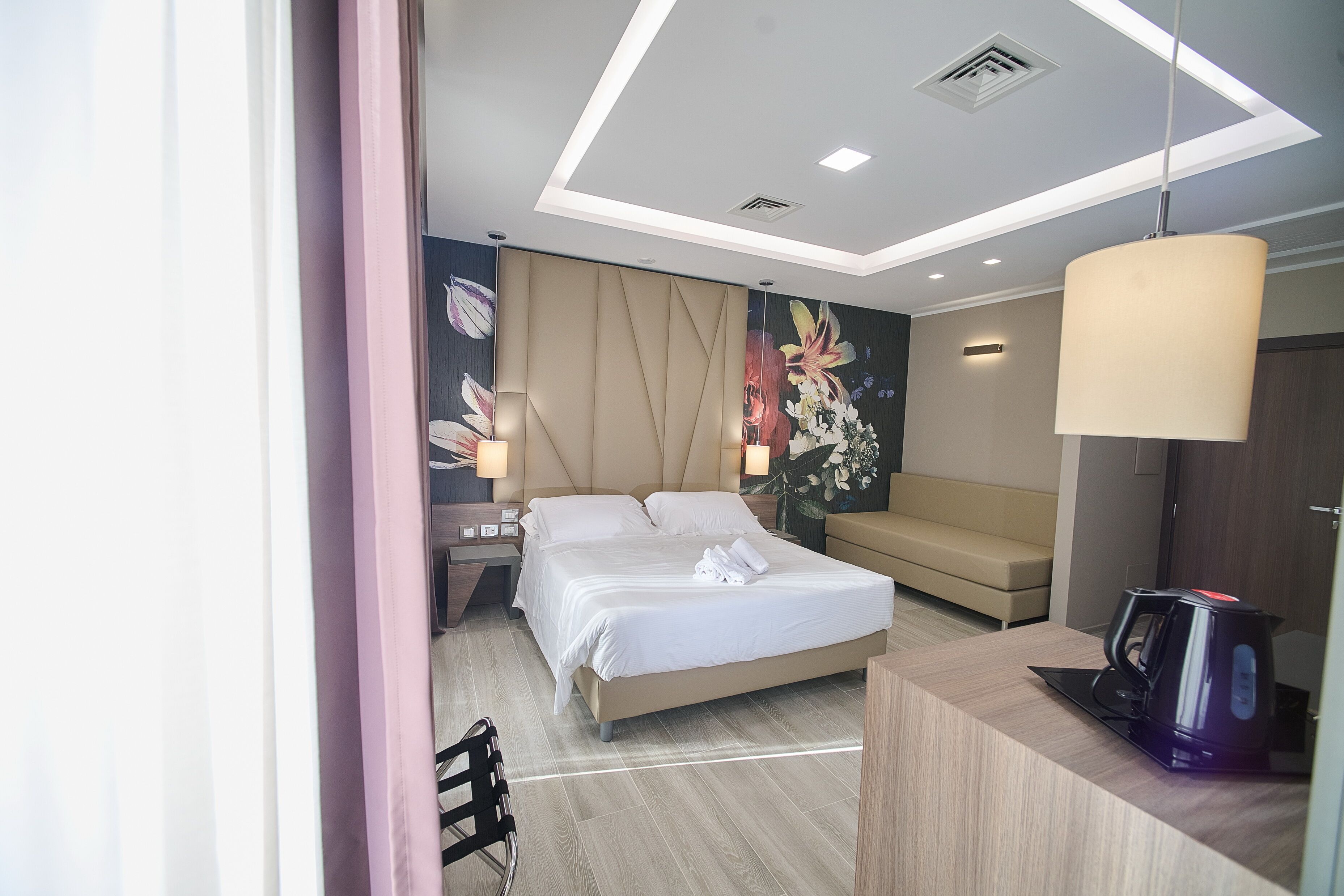 A modern hotel room with a bed, bedside table, lamp, and a desk with a coffee maker.