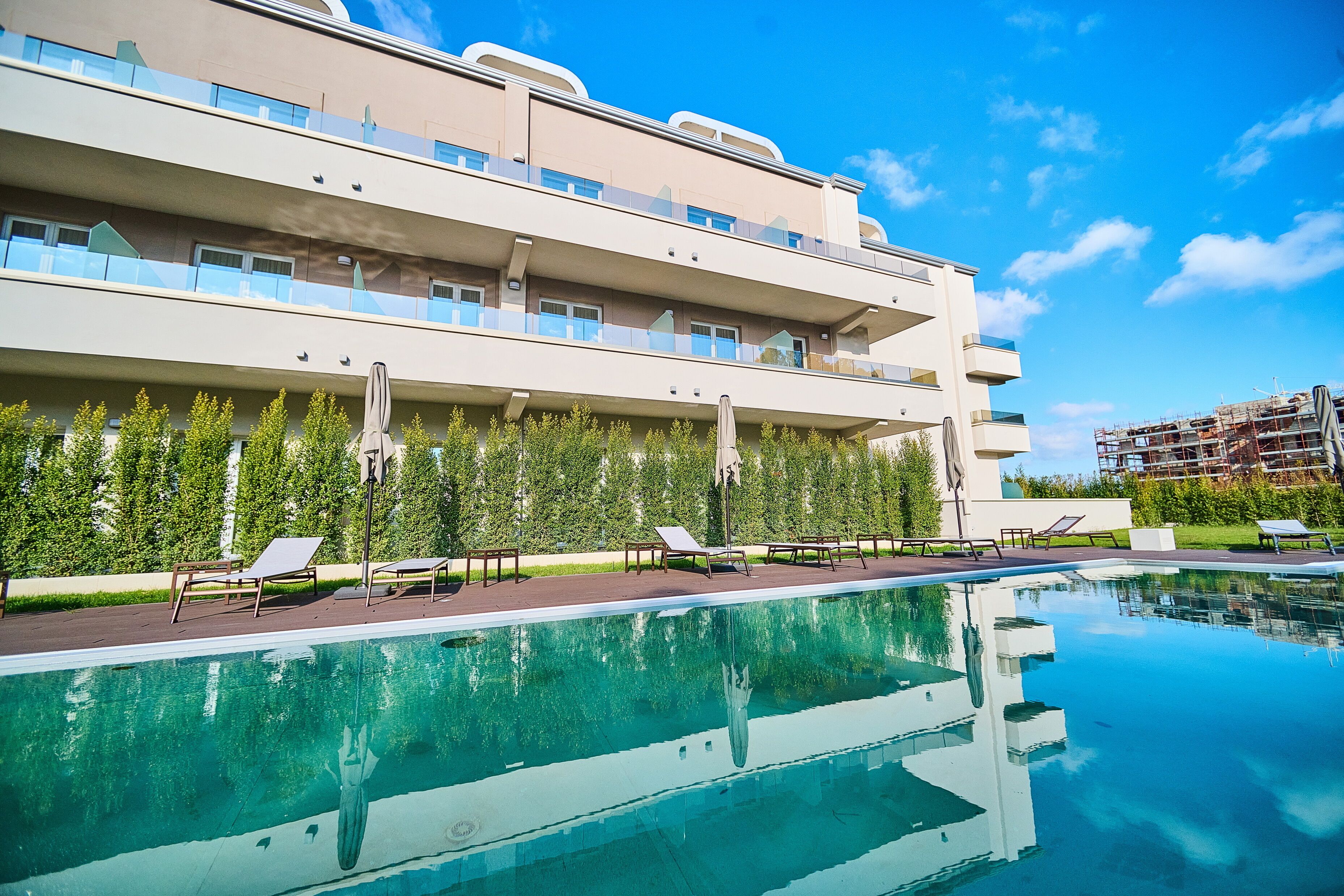Un hotel moderno con piscina, zona de estar exterior y vistas despejadas del entorno verde.
