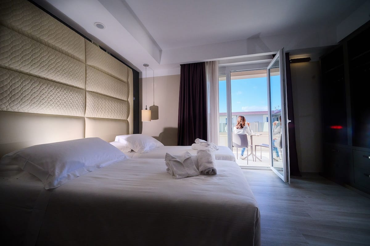 A hotel room with two beds, a large window, and a view of the outside.