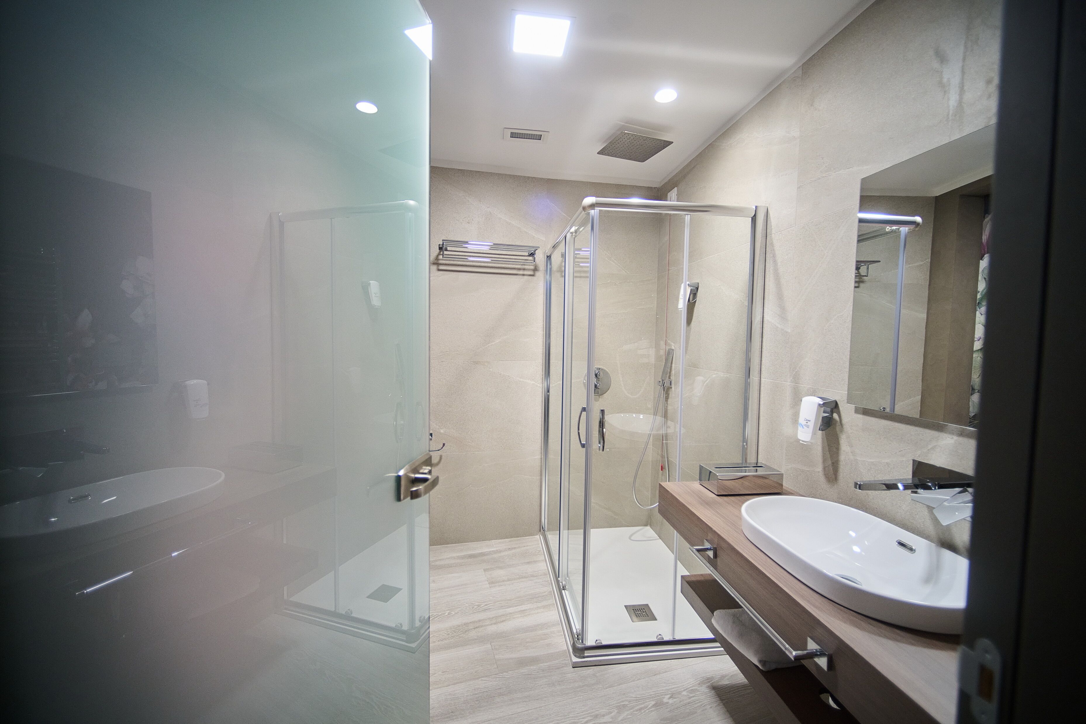 A modern bathroom with a glass-enclosed shower, a large mirror, and a wooden vanity.