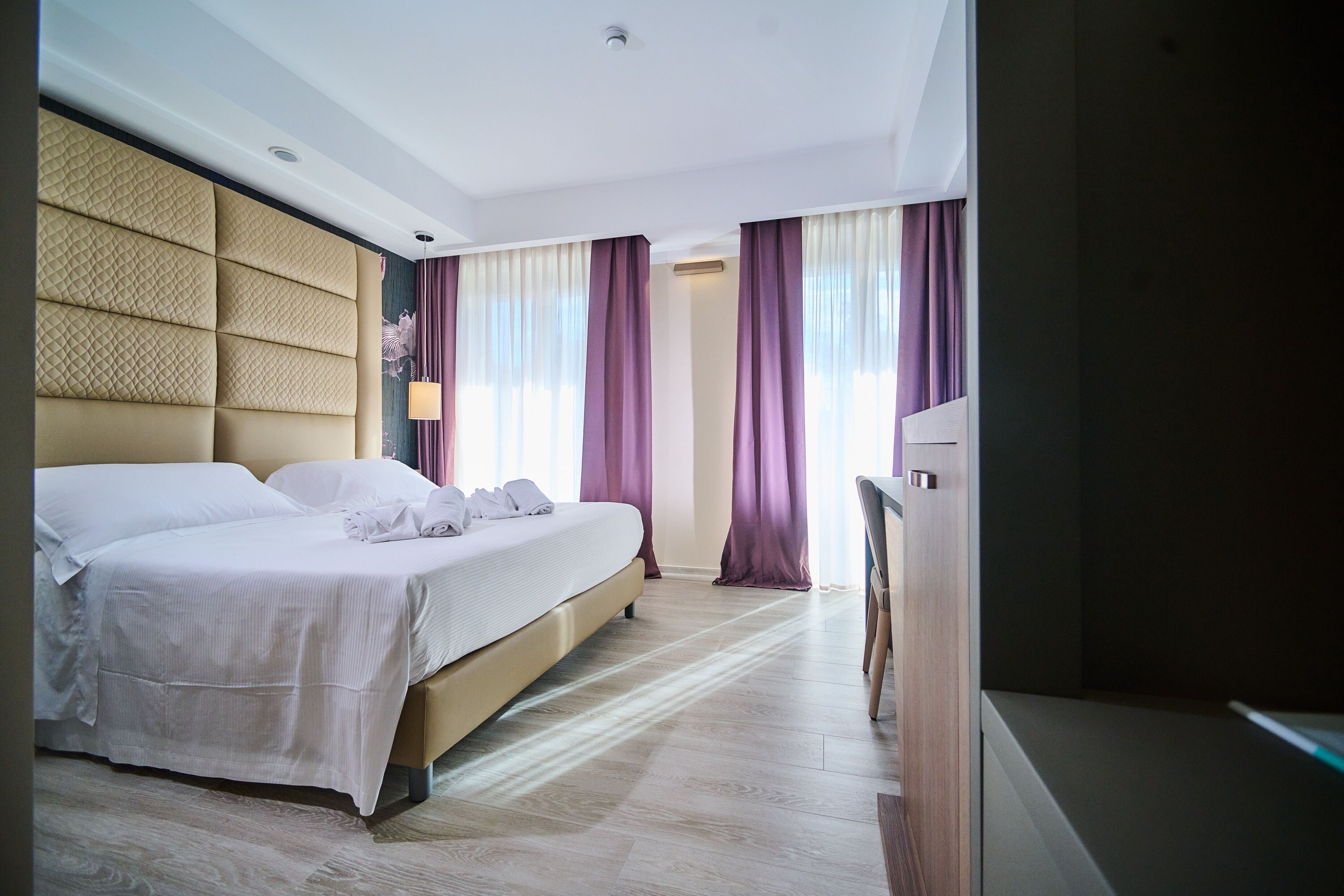 A modern hotel room with a large bed, a flat-screen TV, and a wooden floor.