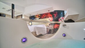 A modern hotel room with a large window, a bed, a desk, and a bathroom with a bathtub. - PARK HOTEL LE DUNE DI GIOVINO (Catanzaro)