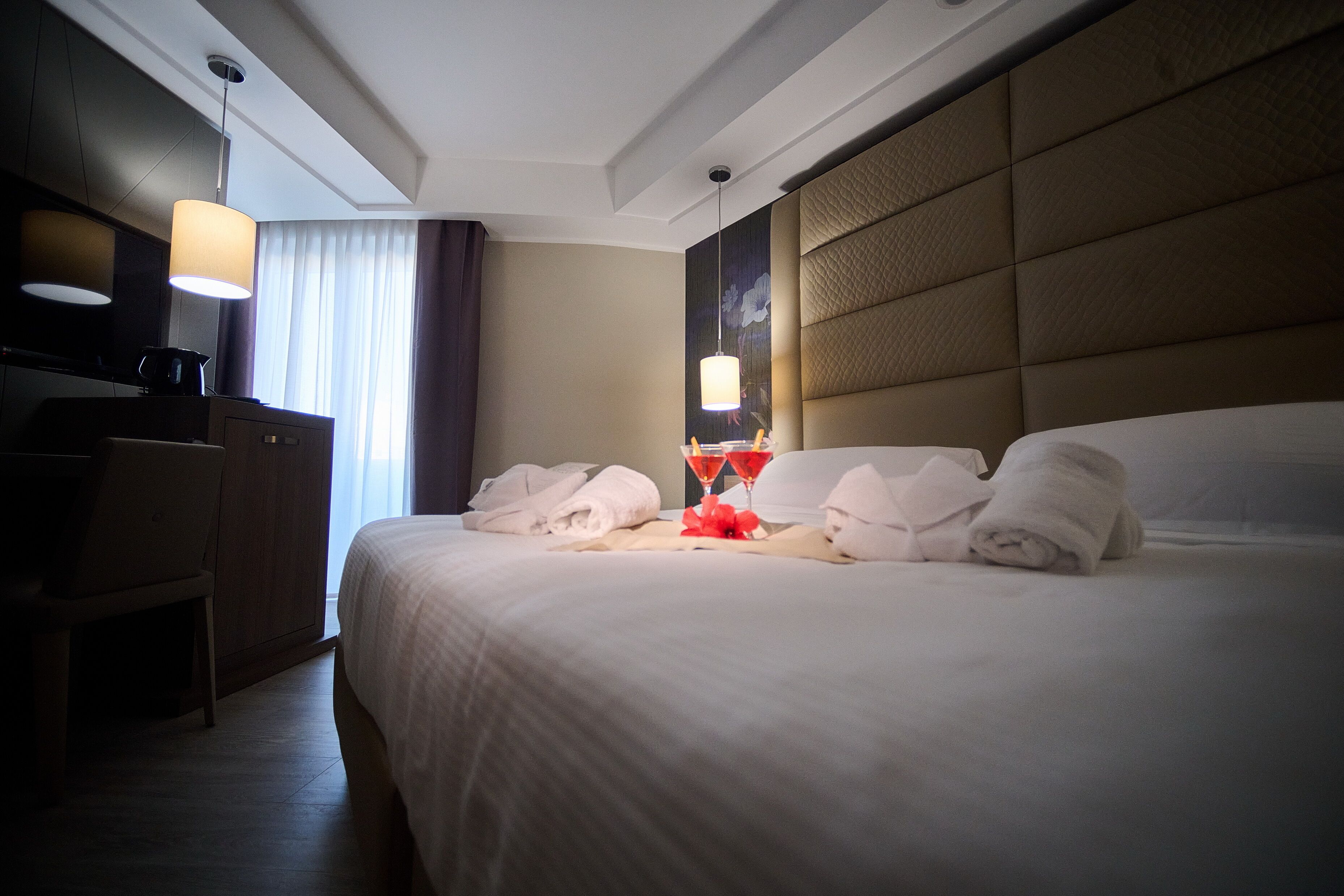A hotel room with a large bed, a desk with a chair, a television, and a lamp.