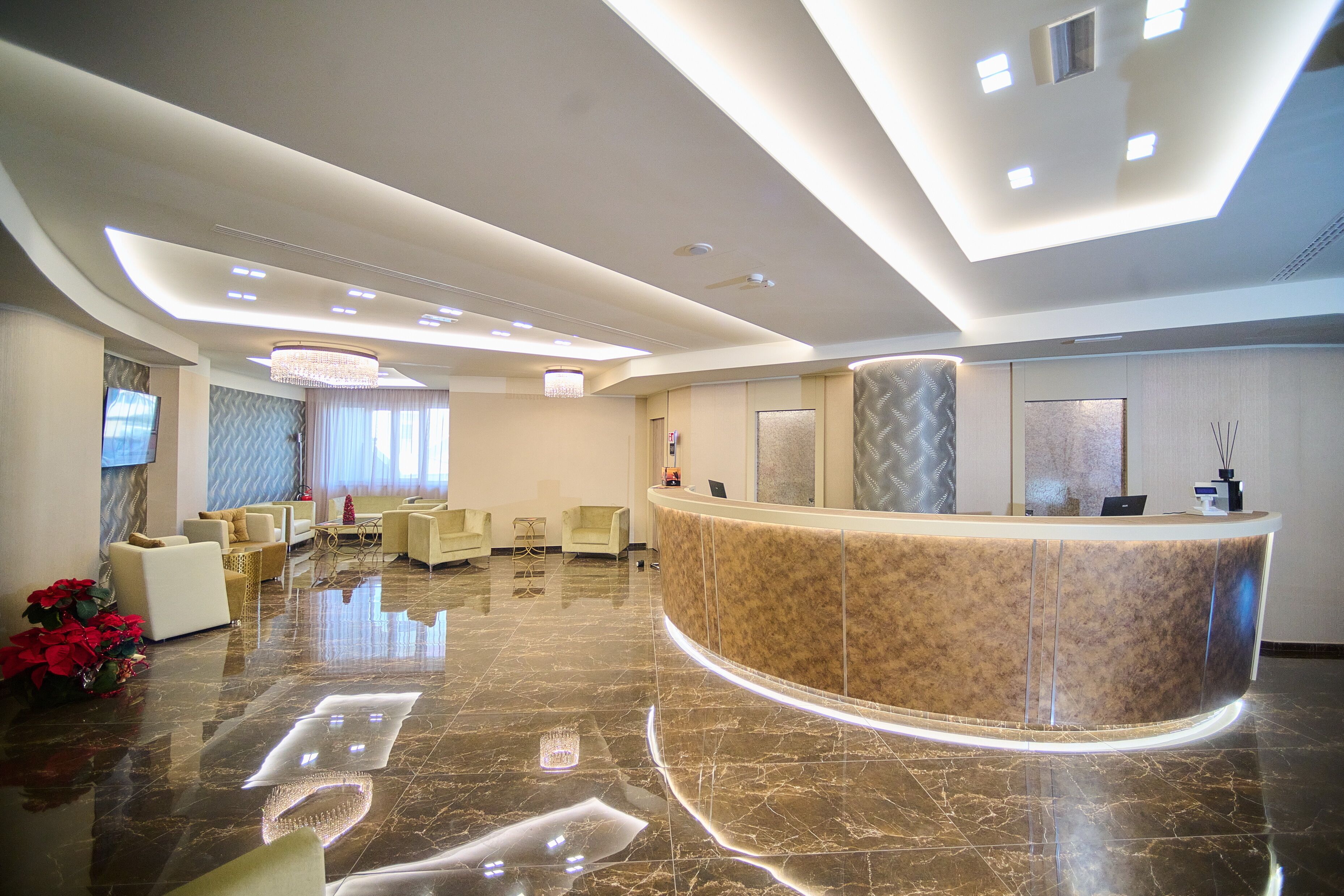 Un hall d’hôtel moderne avec un comptoir d’accueil incurvé, des fauteuils confortables et un lustre.