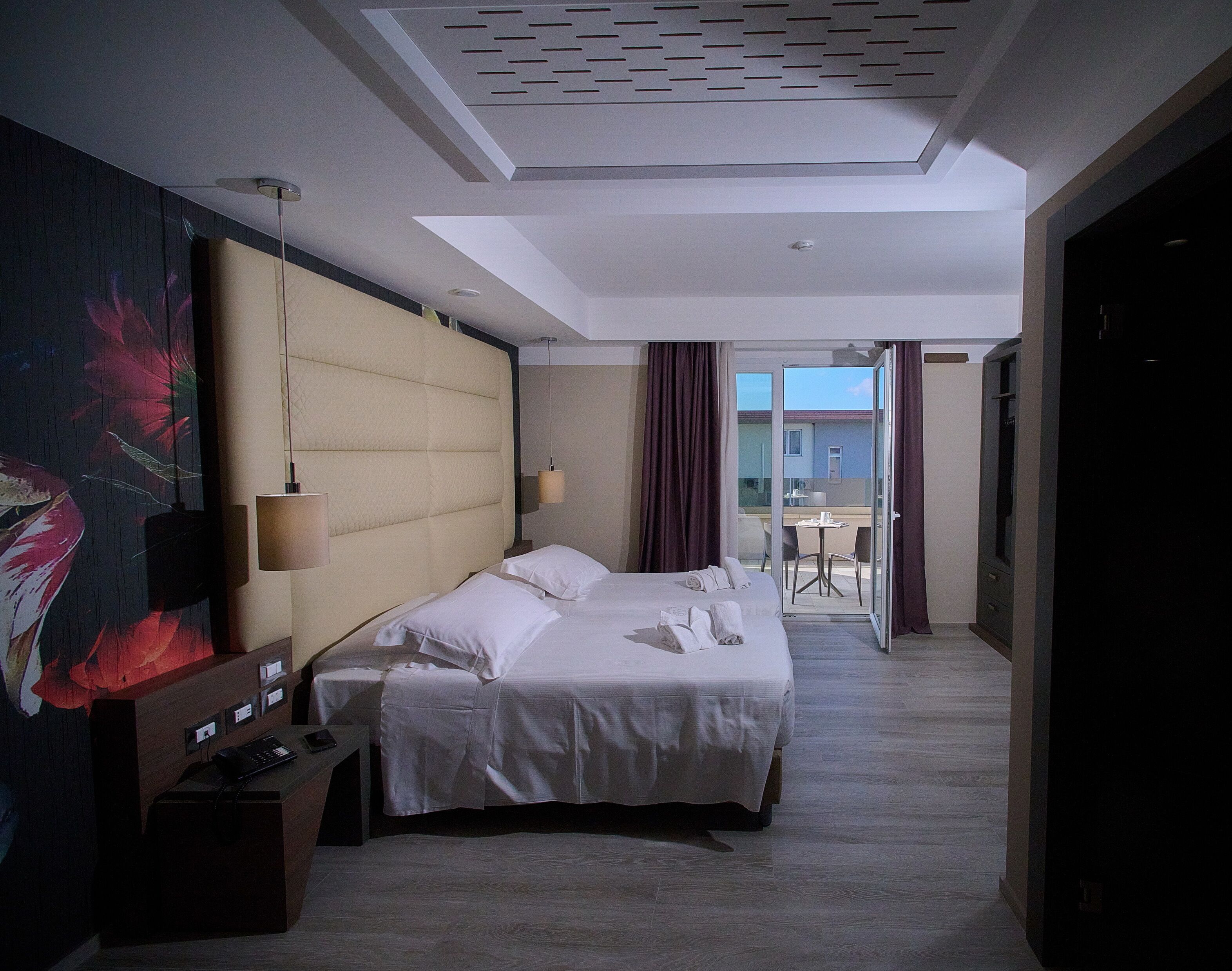 A hotel room with a large bed, a desk with a telephone, and a painting on the wall.