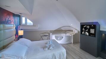 A modern hotel room with a large bed, a small seating area, a bathtub, and a digital information screen.