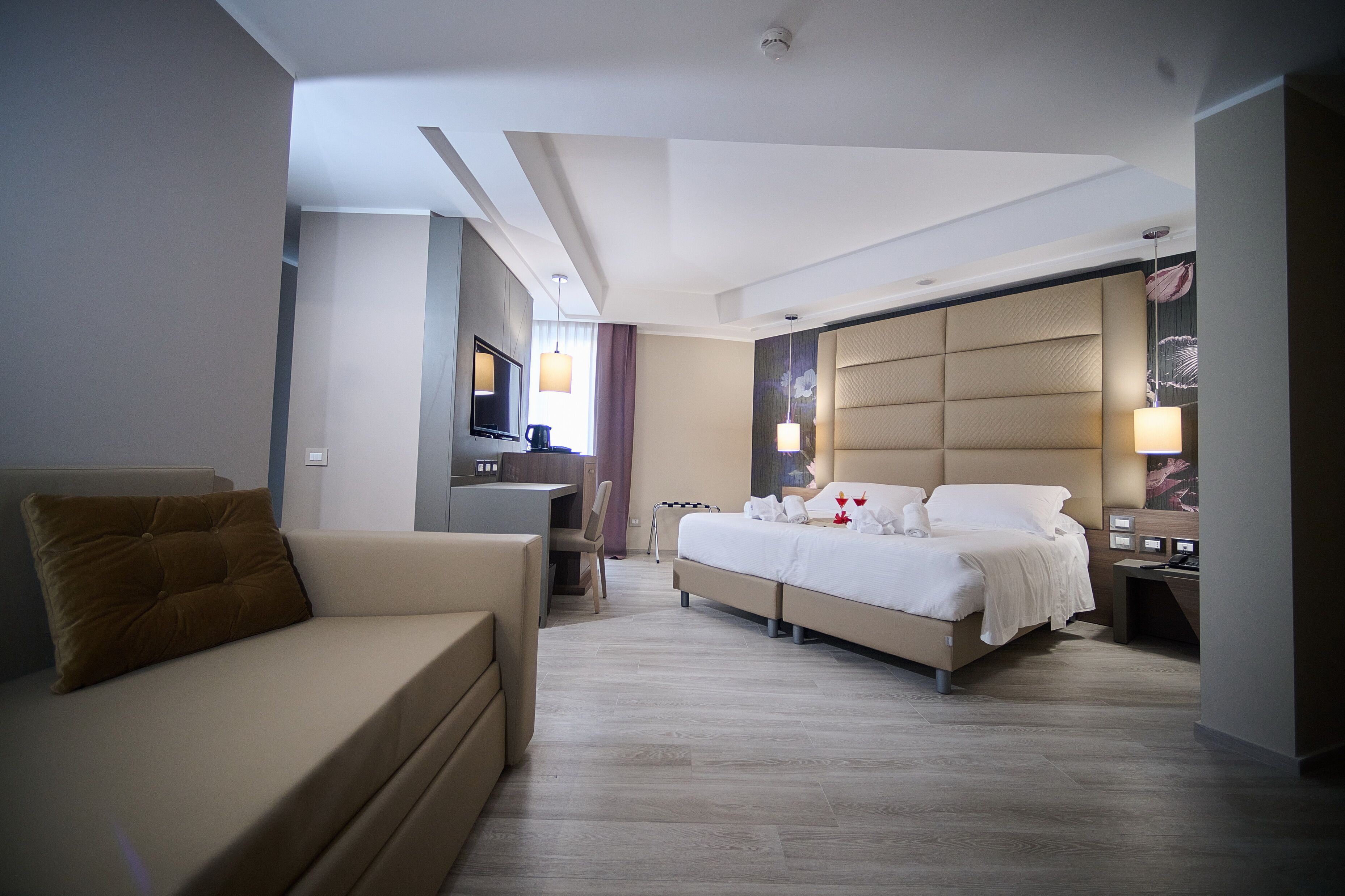 A modern hotel room with a large bed, a sofa, a desk, and a television.