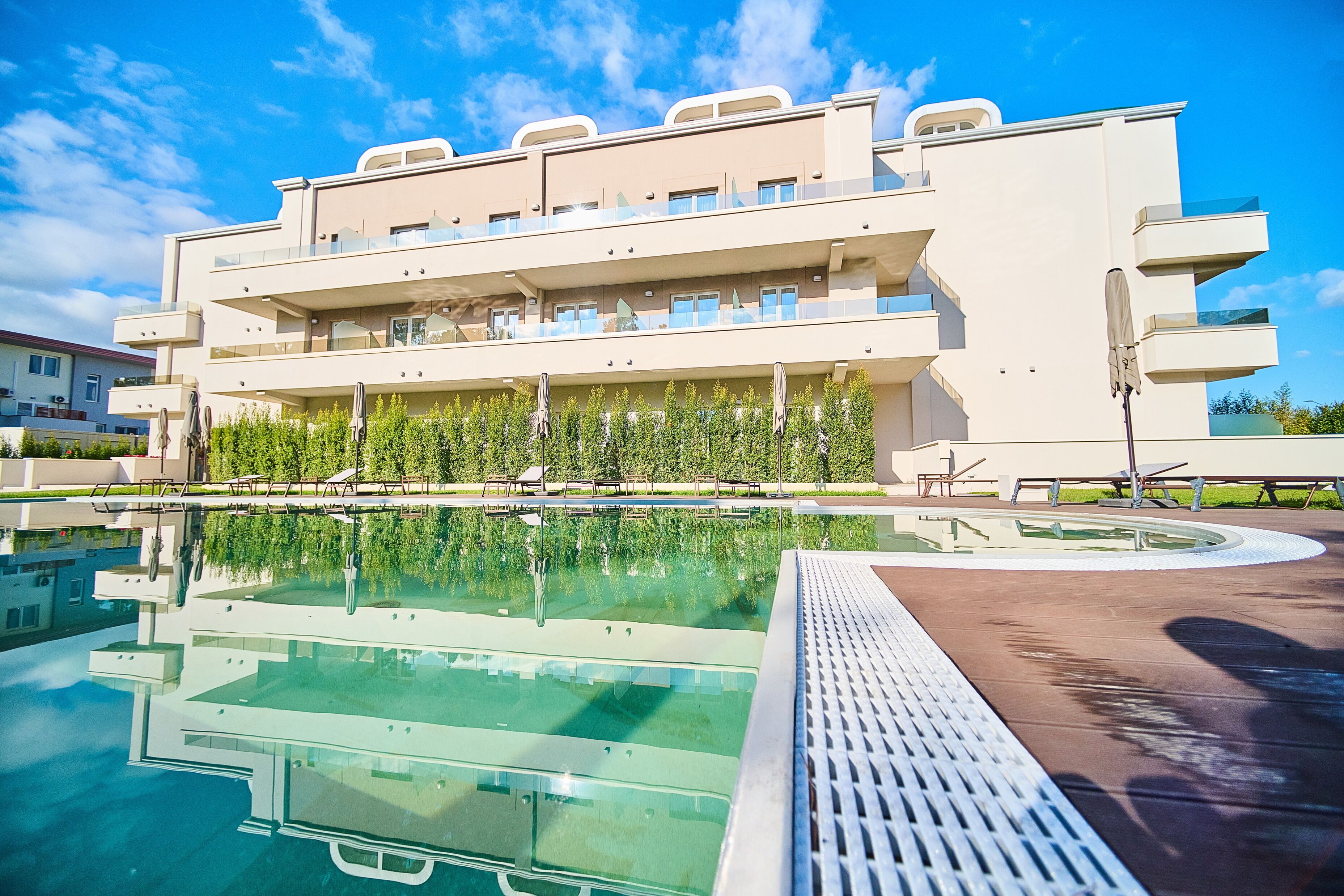 Ein modernes Hotel mit Schwimmbad, mehreren Balkonen und blauem Himmel.