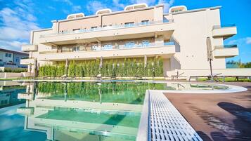 Ein modernes Hotel mit Schwimmbad, mehreren Balkonen und blauem Himmel.
