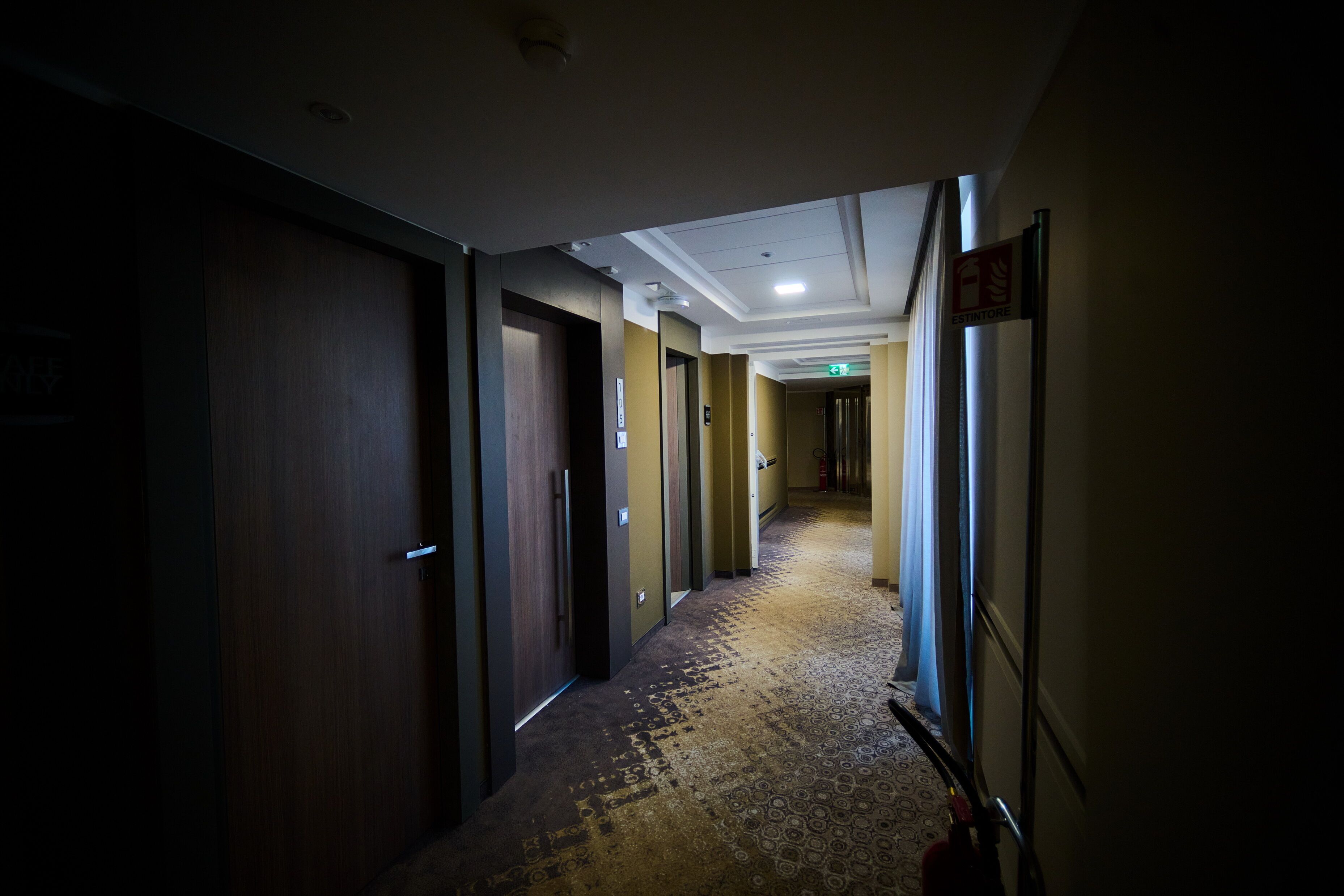 A hotel hallway with wooden doors, a patterned carpet, and a ceiling with recessed lighting.