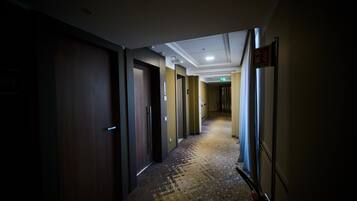 A hotel hallway with wooden doors, a patterned carpet, and a ceiling with recessed lighting.