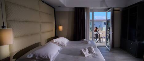 Habitación de hotel con una cama grande, una mesita de noche, una lámpara y vistas al balcón exterior.