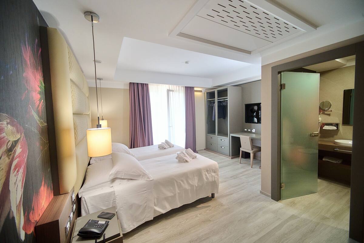 A hotel room with two beds, a desk, a wardrobe, and a bathroom.