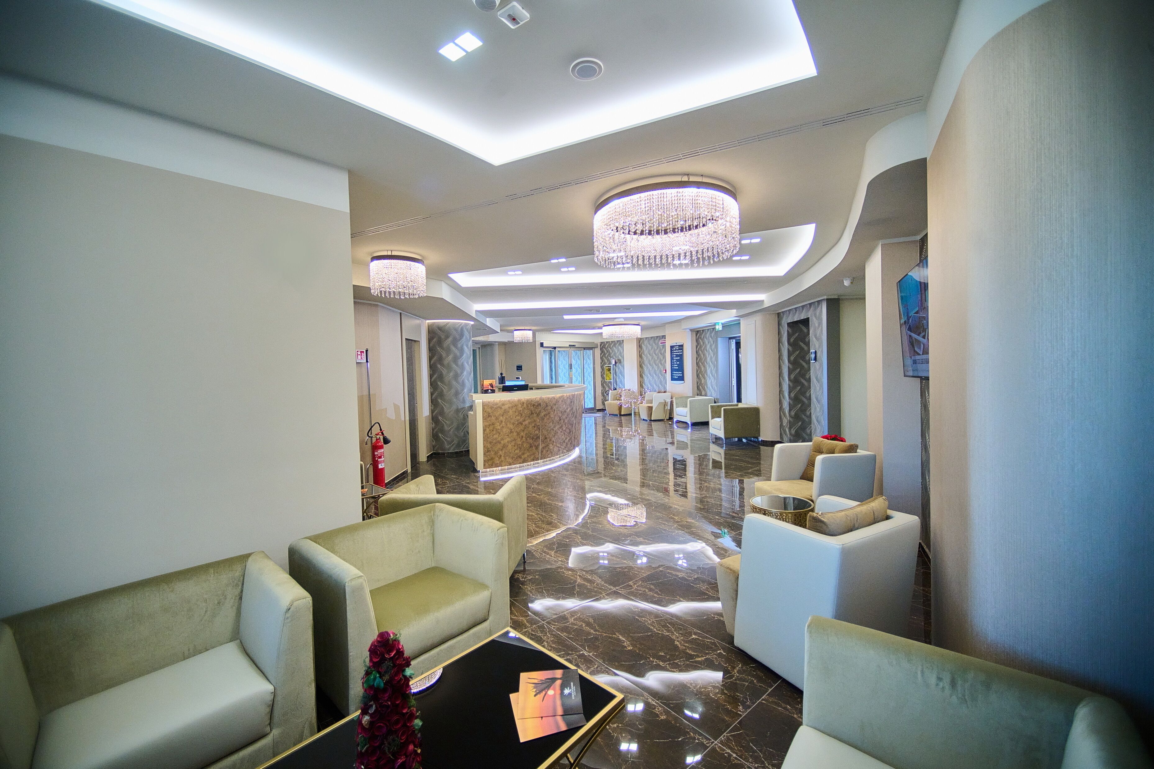 A modern lobby with a reception desk, plush seating, and a chandelier.