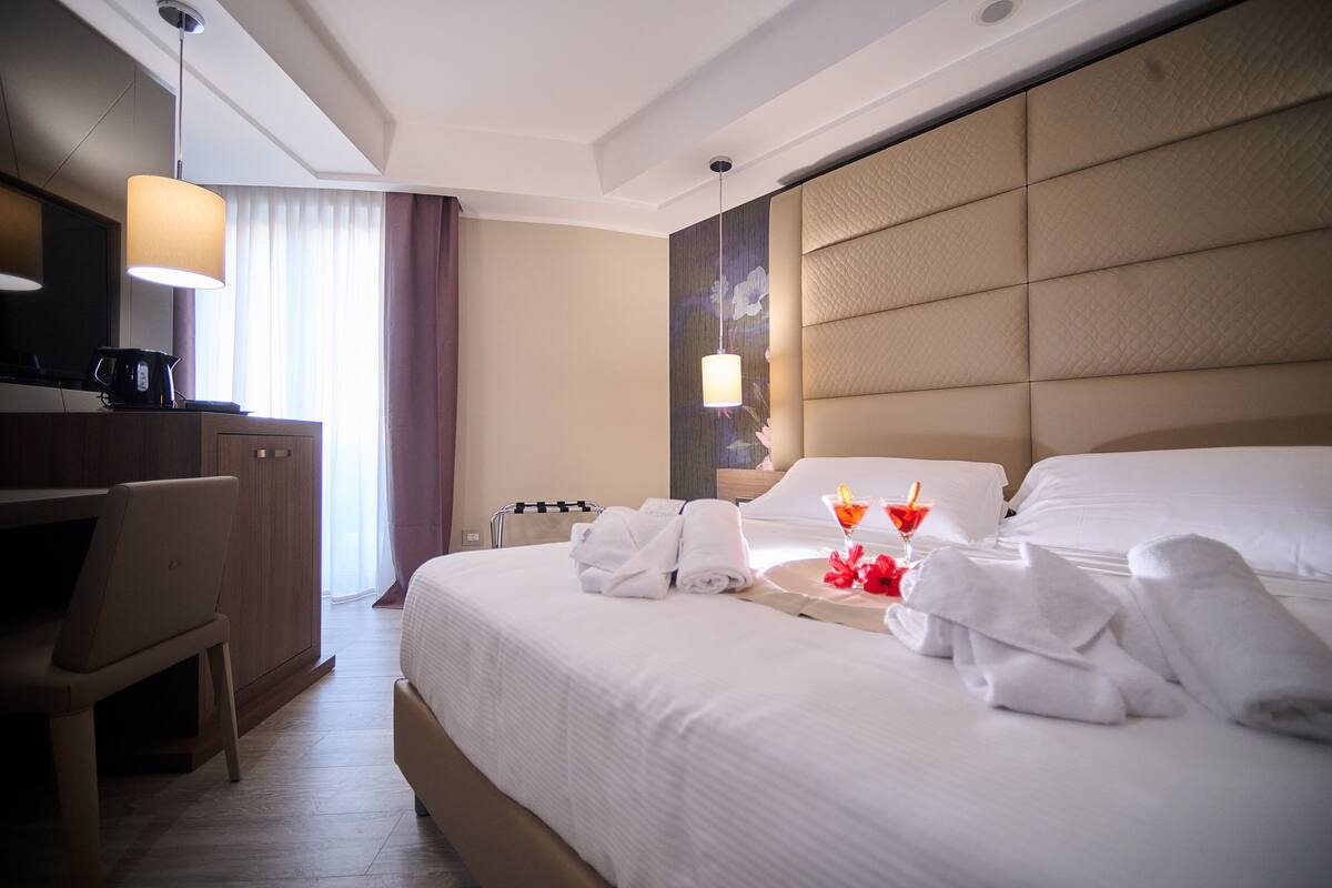 A hotel room with a large bed, a desk with a laptop, a television, and a minibar.