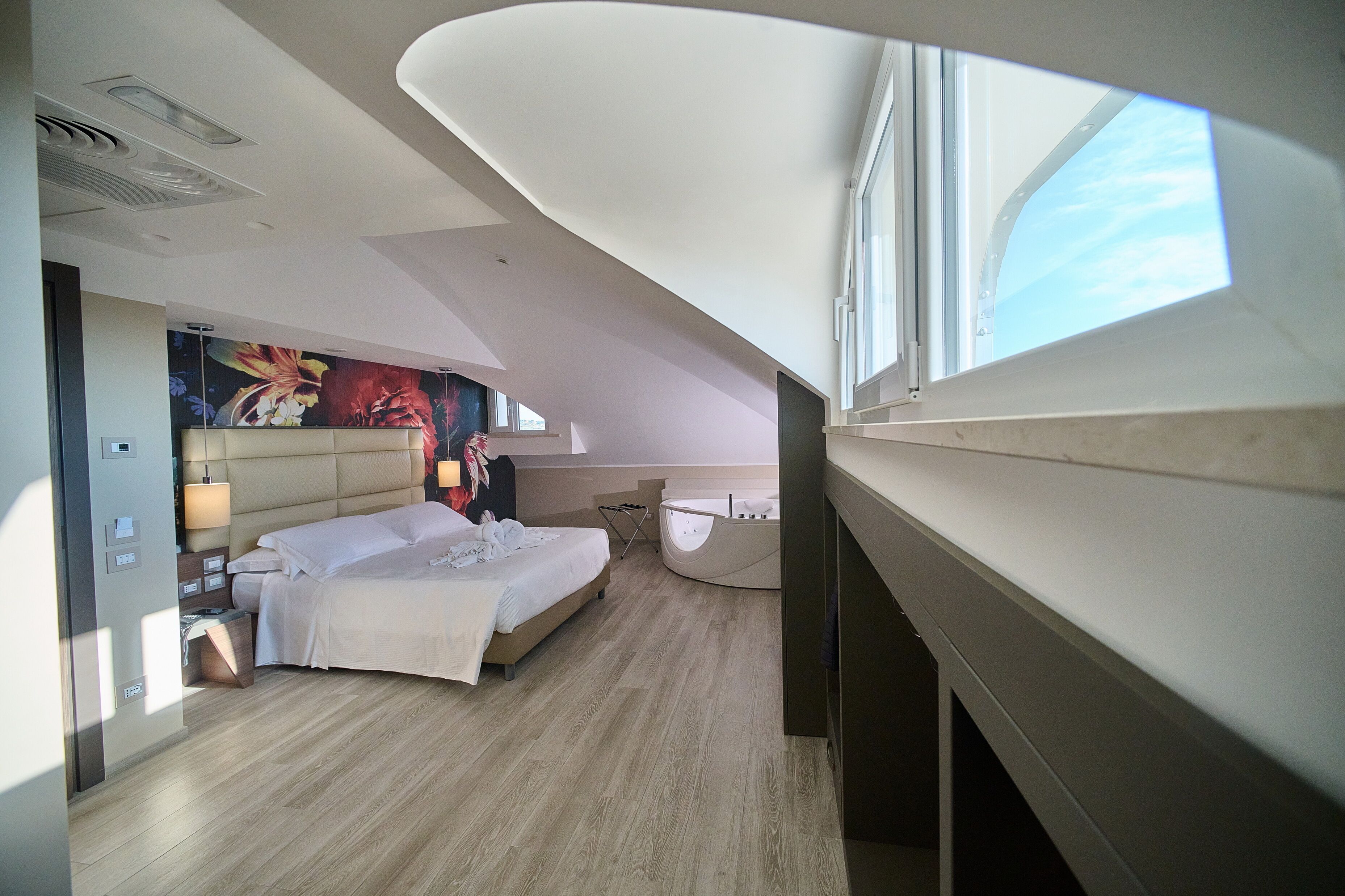 A modern hotel room with a large bed, a bathtub, and a mural on the wall.