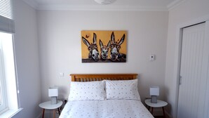 Habitación de hotel con cama, dos mesitas de noche, un cuadro colgado en la pared de burros y una ventana con persianas.