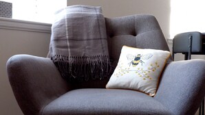 Un sillón gris con un cojín con diseño de abeja, un espejo con forma de corazón y una manta gris.