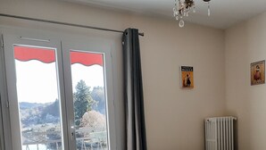Habitación de hotel con cama, radiador, araña y vista a un lago a través de un ventanal.
