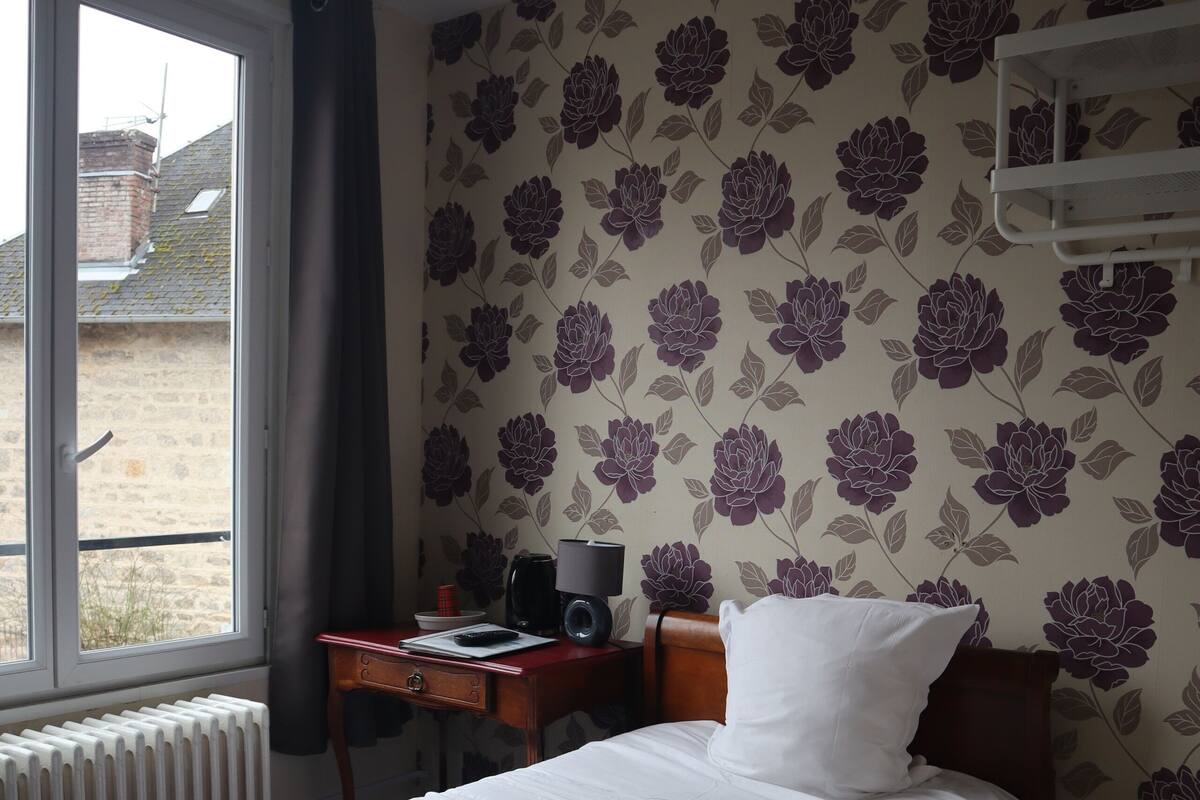 A room with a bed, a desk, a radiator, and a window with curtains.