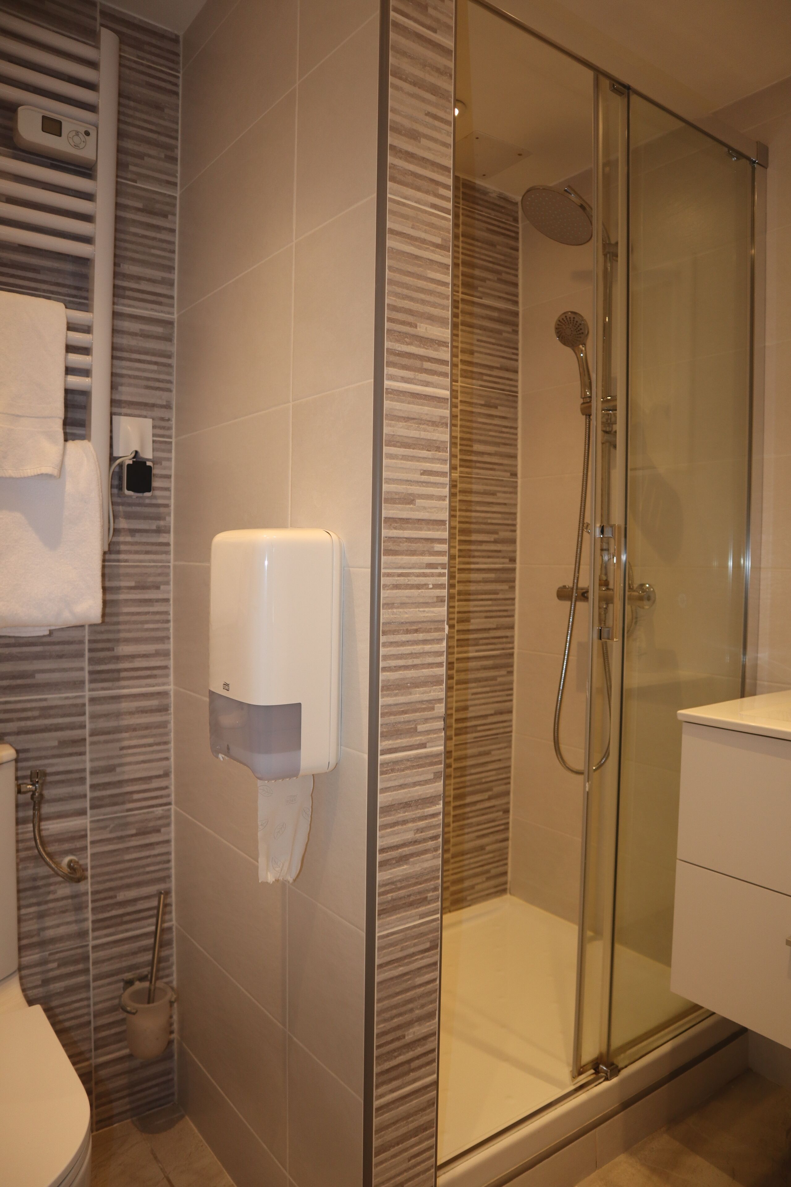 A modern bathroom with a glass-enclosed shower, a hand dryer, and a toilet.