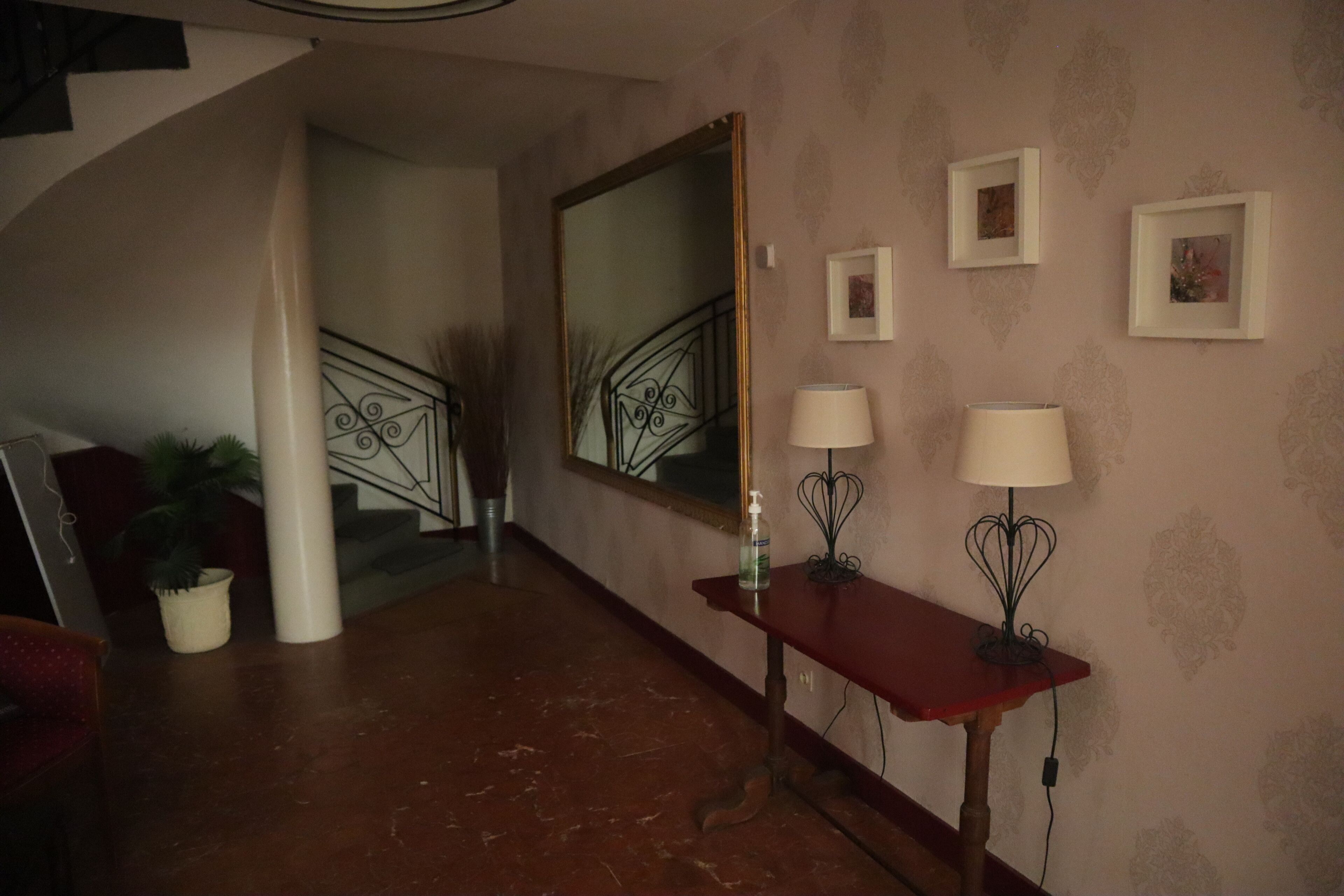 A hallway with a marble floor, a red console table with two lamps, a large mirror, and framed pictures on the wall.