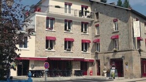 Hotel con restaurante y bar en la planta baja, con fachada de piedra y toldos rojos.
