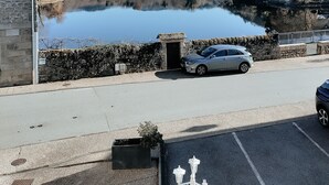 Un estacionamiento con un edificio de piedra, un automóvil y vista a un lago rodeado de árboles y colinas al fondo.