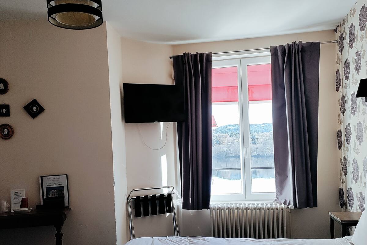 A hotel room with a bed, a flat-screen TV mounted on the wall, a window with curtains, a radiator, and a ceiling fan.